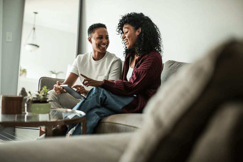 two people site on a couch looking at a tablet