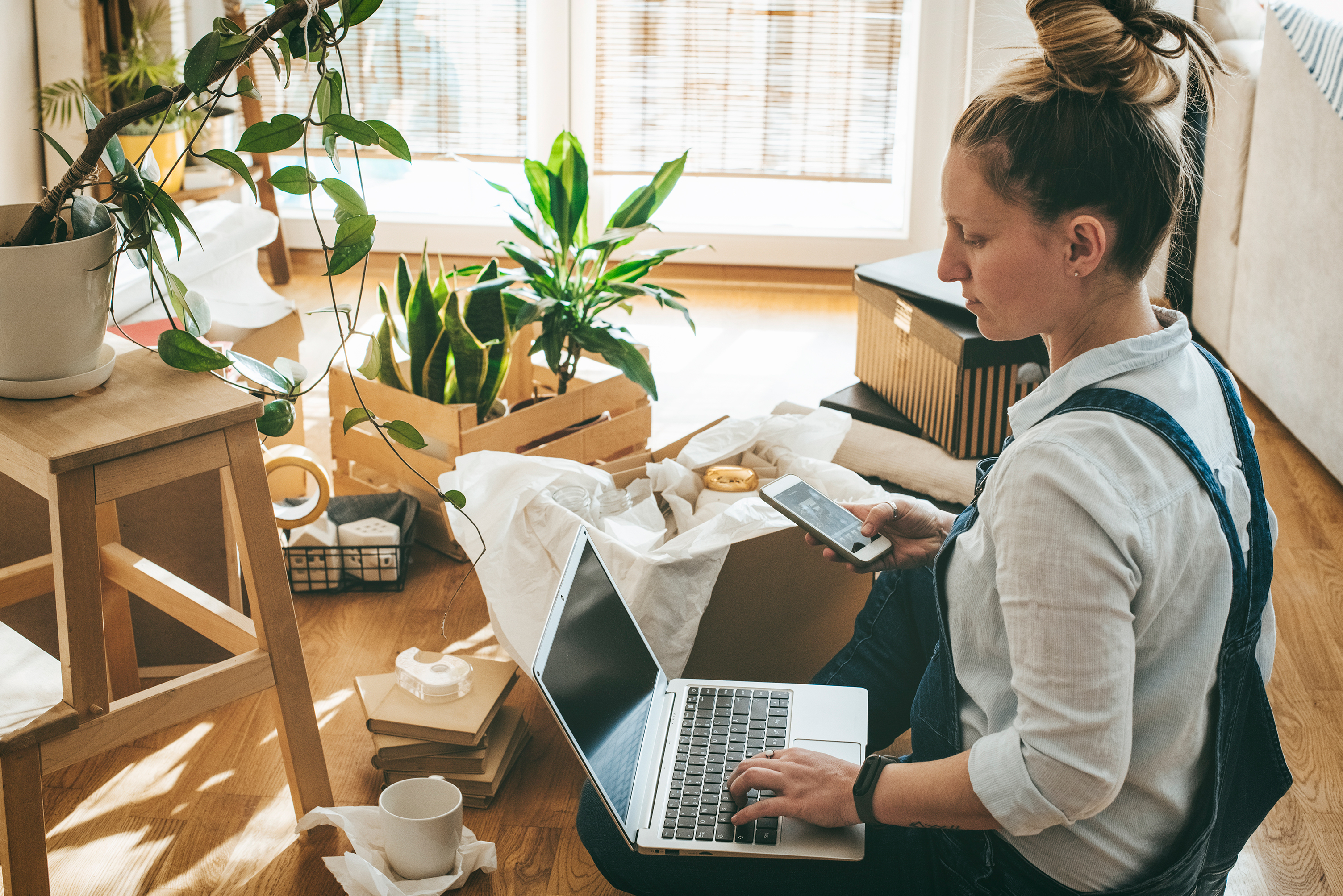 A woman uses a smartphone and laptop to look at her finances.