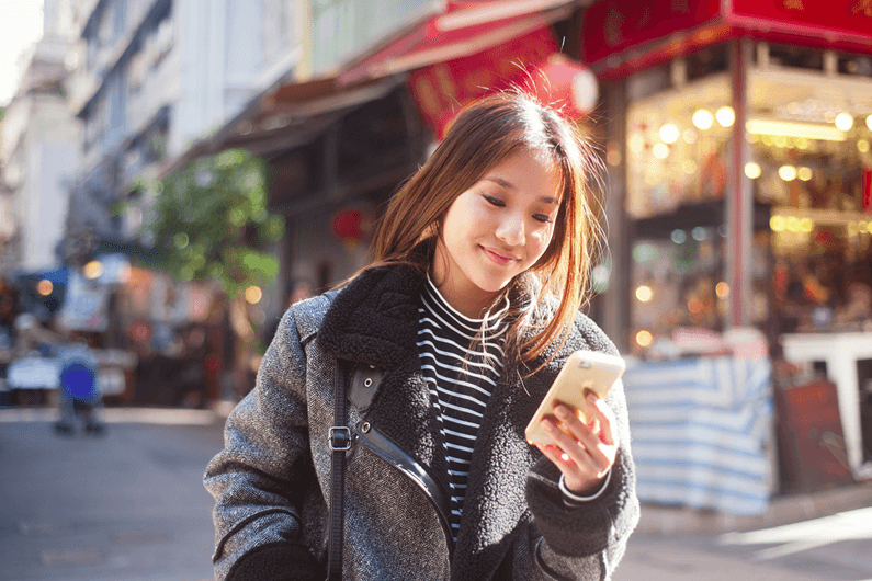 a woman smiles at the phone in her hand as she stands on the street