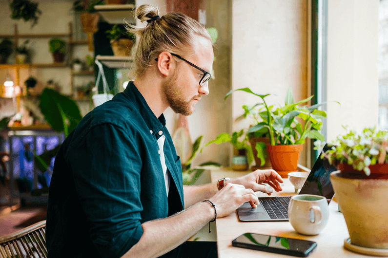 a man with glasses sits at a desk working on a laptop