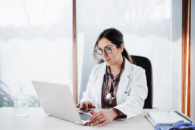 A physician sits with a laptop computer and researches how to apply for a physician mortgage.