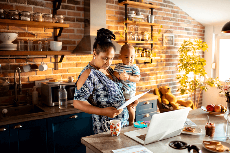 Woman holding an infant in a kitchen while researching ways to save money on a tight budget through Fifth Third Bank.