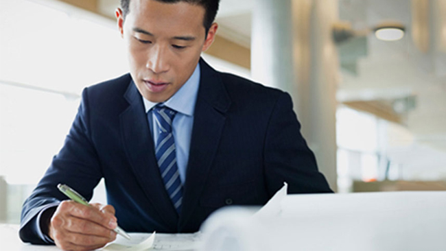 A male business owner wearing a suit reviews paper documents in a brightly lit office space.